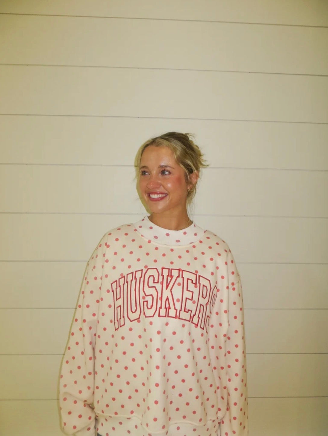 Woman modeling a white Nebraska Huskers polka dot mockneck sweatshirt with red collegiate HUSKERS lettering and an oversized fit.