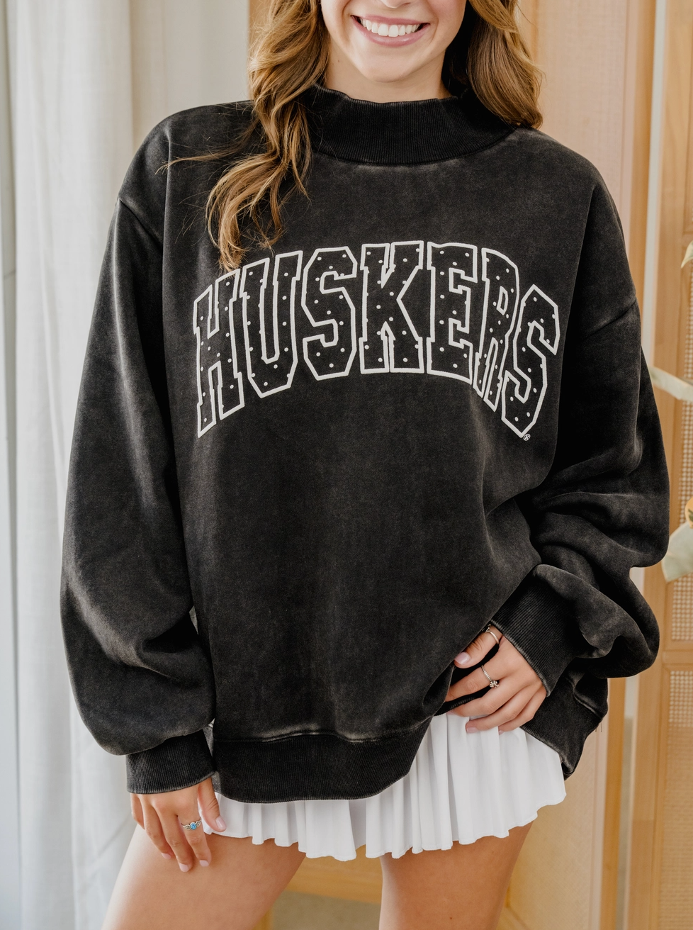 Model wearing black Nebraska Huskers mockneck sweatshirt with white HUSKERS graphic