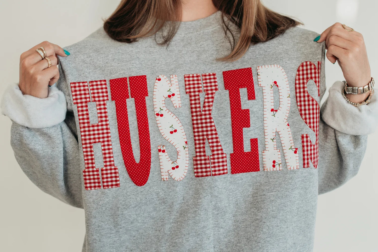 Model wearing a retro gray Nebraska Huskers crewneck sweatshirt with red gingham and white heart-pattern HUSKERS lettering.