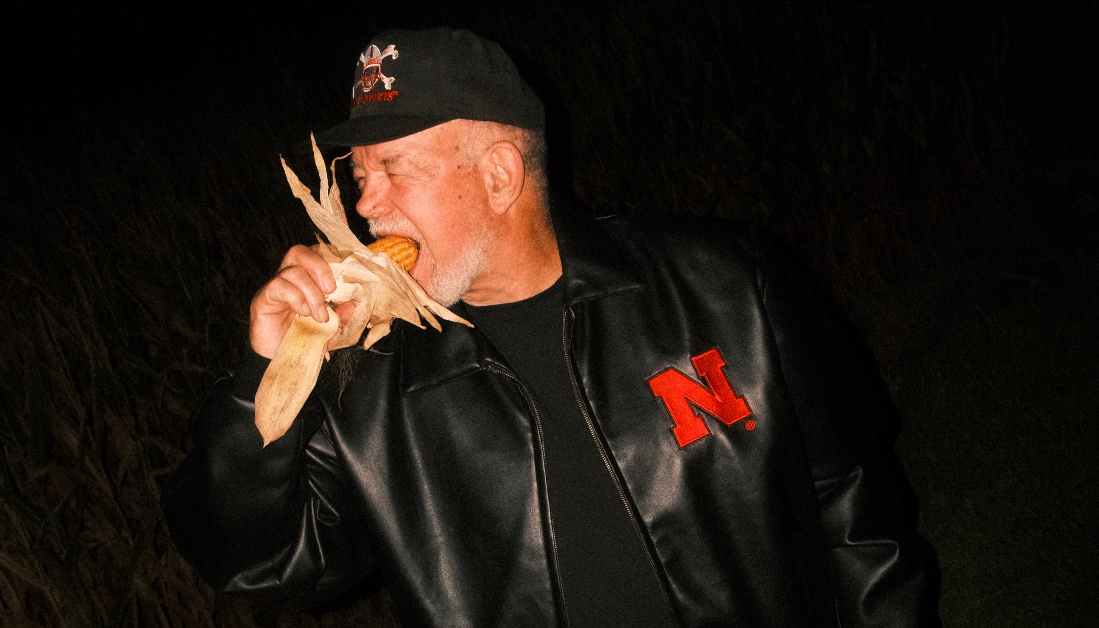 Man eats corn in cornfield wearing old Husker clothing