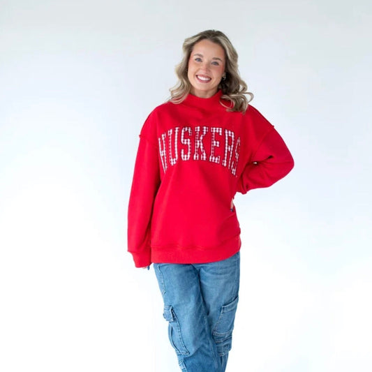 Woman wearing a Nebraska Huskers red mockneck sweatshirt with white gingham arched HUSKERS lettering and a relaxed oversized fit.