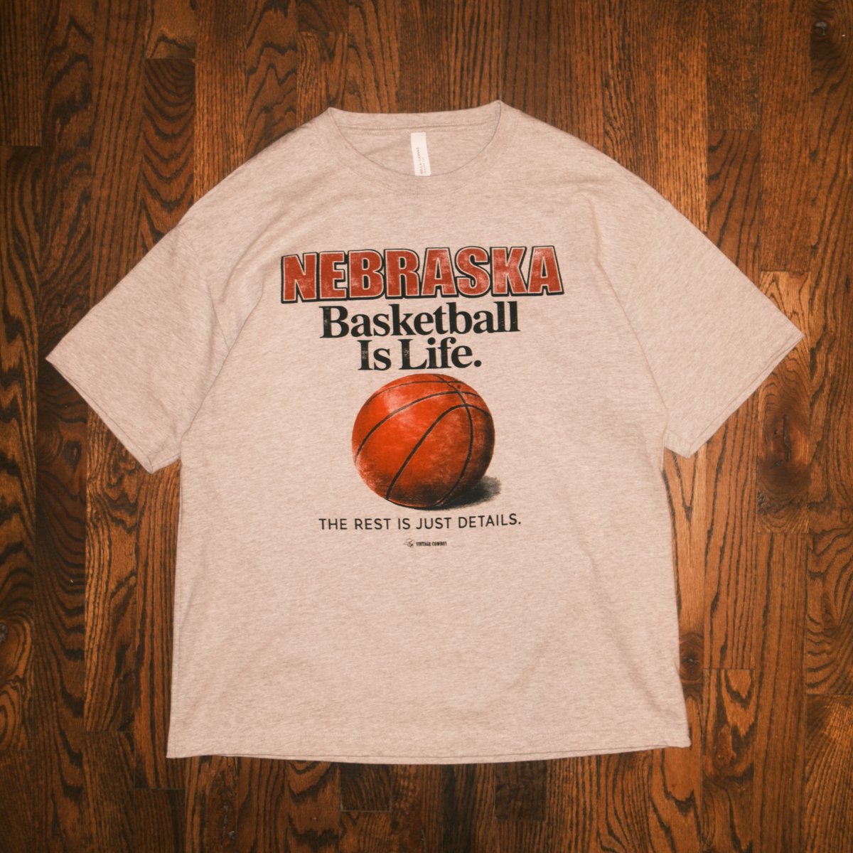 Grey Nebraska Basketball Is Life graphic t-shirt laid flat on a wood floor