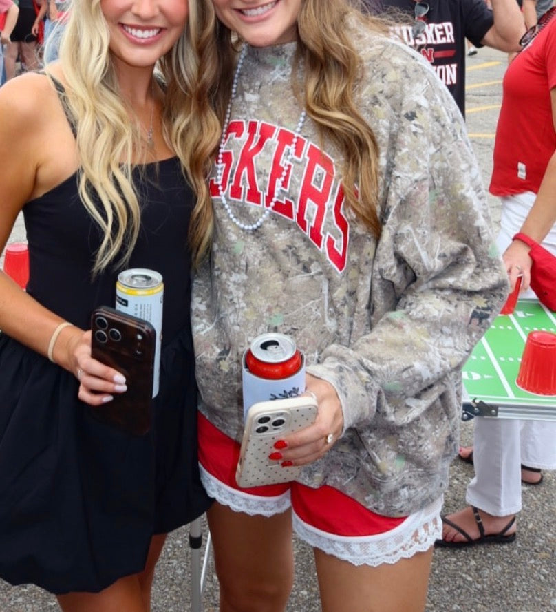 Woman wearing an oversized Nebraska Huskers camo mockneck sweatshirt with red HUSKERS lettering at a Husker gameday.