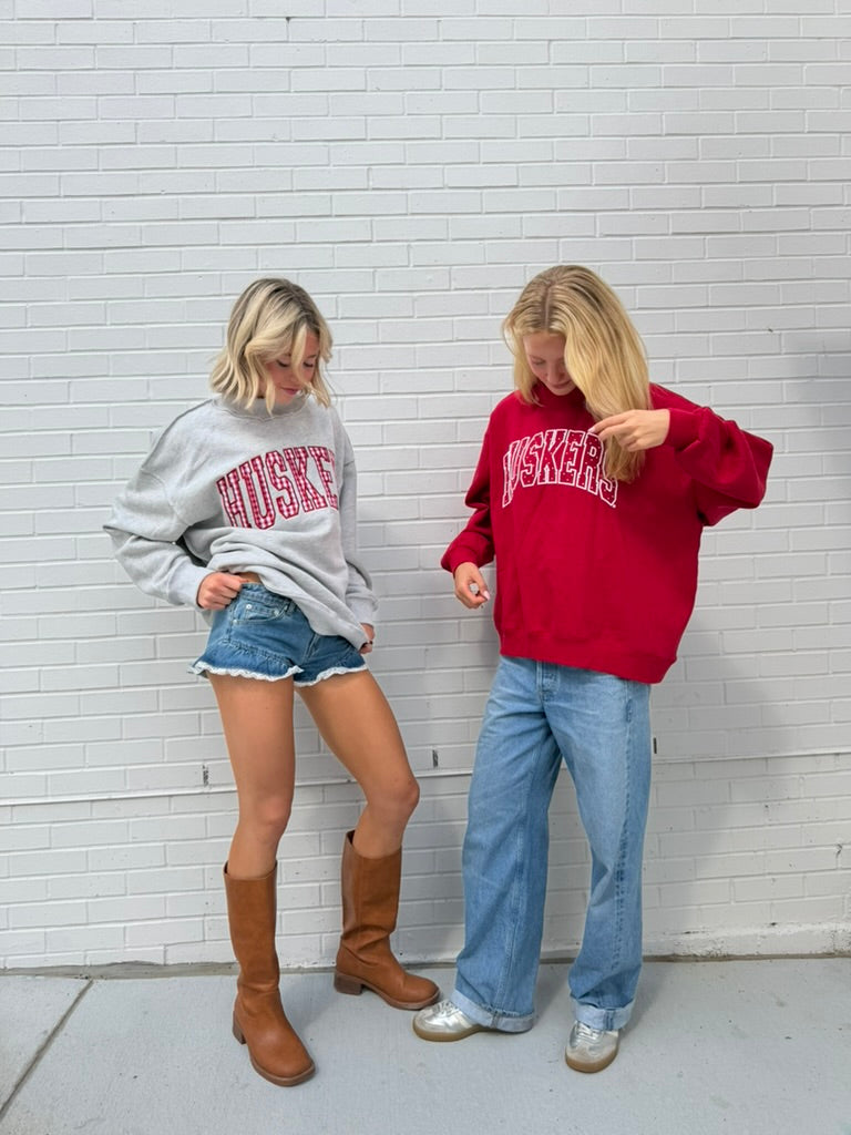 Two models wearing gray and red Nebraska Huskers mockneck sweatshirts outdoors