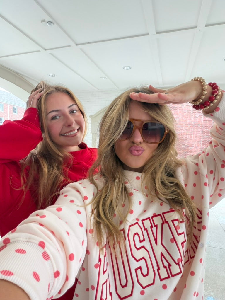 Two models wearing retro Nebraska Huskers mockneck sweatshirts including the white red polka dot style