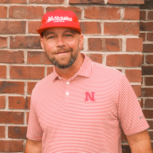Man wearing a red Nebraska Lincoln script hat with a red and white striped Nebraska polo
