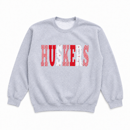 Retro gray Nebraska Huskers crewneck sweatshirt with red gingham, solid red, and white heart-pattern HUSKERS lettering.