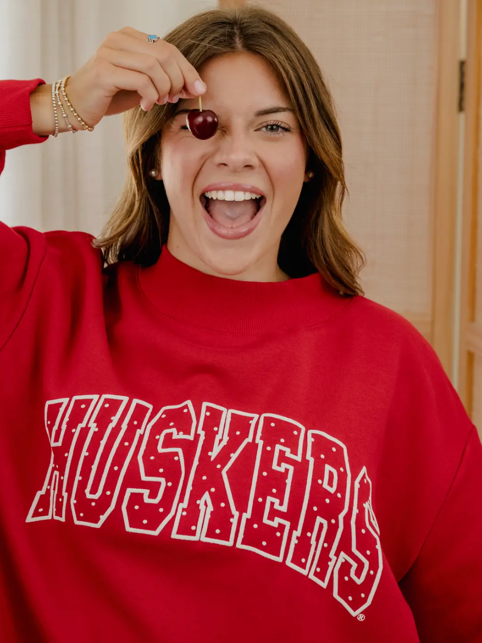 Model wearing a retro red Nebraska Huskers mockneck sweatshirt with white polka dot HUSKERS lettering.
