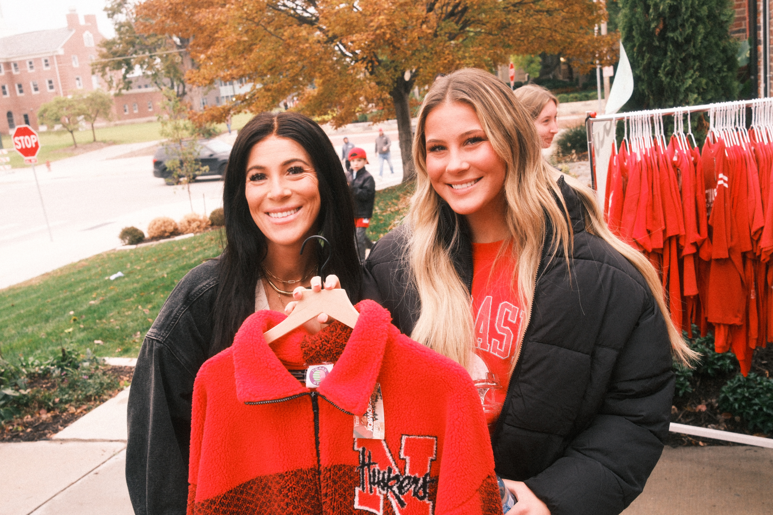 Two shoppers holding a red vintage Nebraska Huskers jacket at a Vintage Cowboy pop-up event