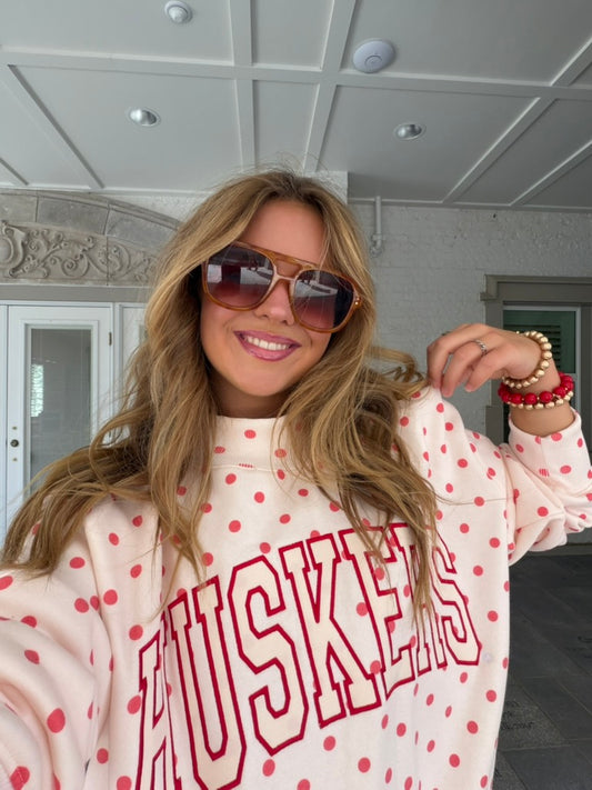 Model wearing a white Nebraska Huskers mockneck sweatshirt with red polka dots